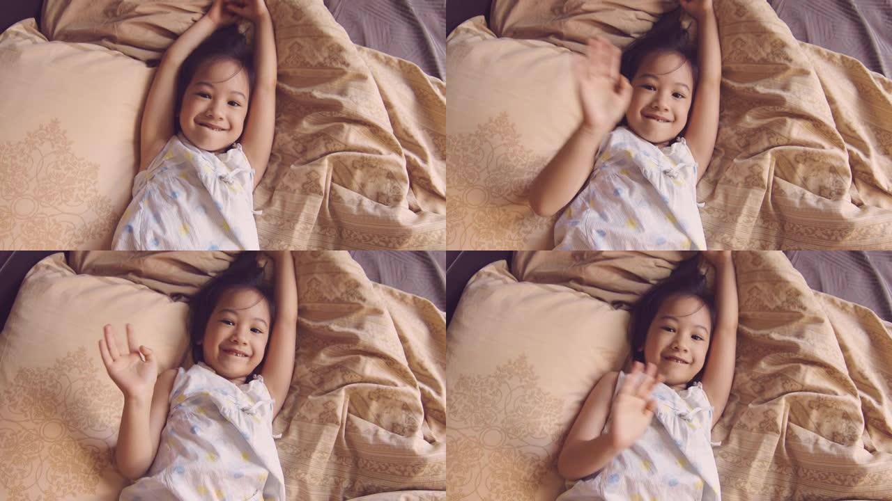 穿着睡衣的白色皮肤可爱的亚洲小孩的肖像，早上在床上对着镜头，阳光透过窗户照射。她的眼神交流表达了喜悦