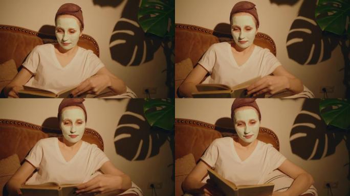 美国妇女正在沙发上读书，并在面部spbas上戴着化妆品面膜