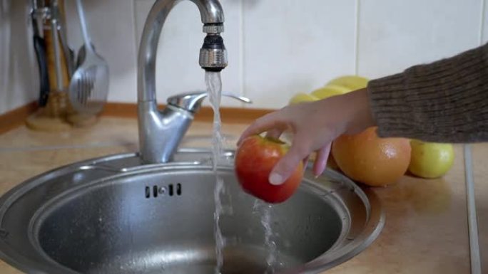 女人用厨房的水龙头用流水冲洗成熟的红苹果