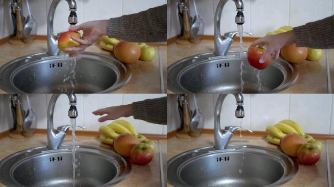 女人用厨房的水龙头用流水冲洗成熟的红苹果