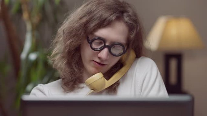 智能集中20世纪80年代男子在黄色老式电话上聊天的肖像，室内坐着复古笔记本电脑。天才高加索年轻人在家