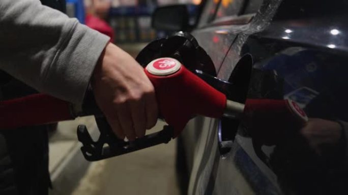 一个人手中的加油枪插入汽车的油箱中。