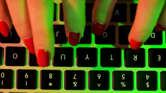 一个有着红色修指甲的女孩的手的俯视图，在笔记本电脑上打字，写电子邮件，浏览互联网。在绿色霓虹灯下在计