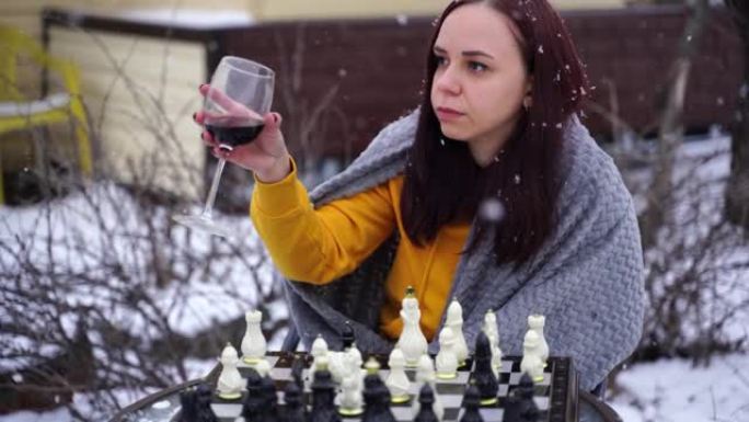年轻女子在院子里下棋。冬季穿着灰色格子的女性坐在街上玩棋盘游戏
