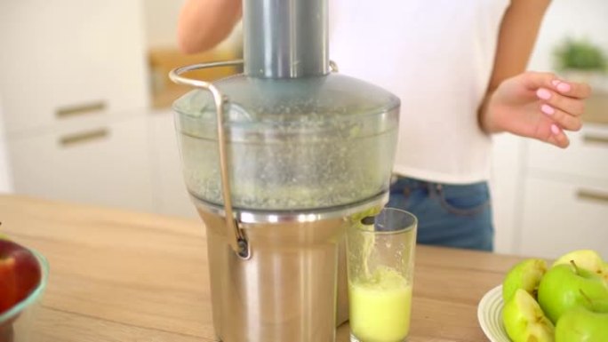 女人在榨汁机上制作苹果汁，然后在厨房的家中新鲜饮用。榨汁和健康饮食快乐的女人制作绿色蔬菜和果汁