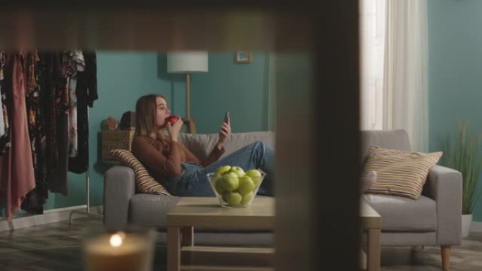 美女吃红苹果，躺在沙发上，通过视频链接说话