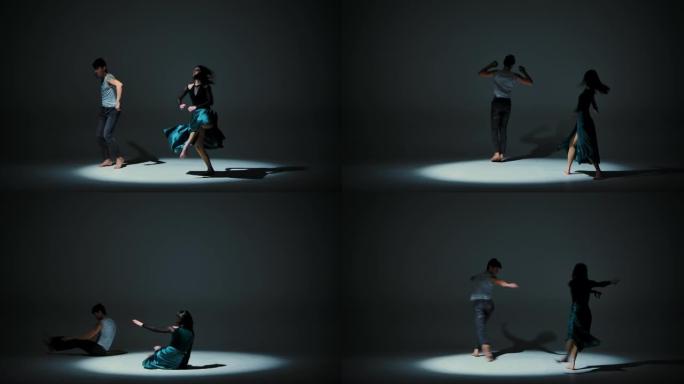 在深灰色工作室背景下练习元素现代当代风格的双人舞者的情感表现。男人和女人在旋转，优雅地跳跃，跳舞现代