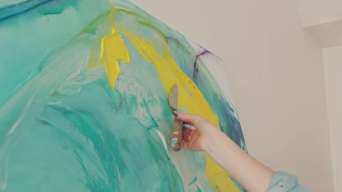 才华横溢的女艺术家在抽象图案上涂上黄漆和抹刀。年轻女子在工作场所画架上画画。特写。