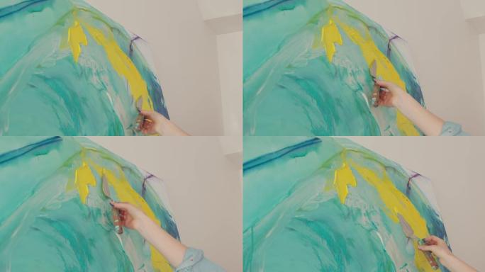 才华横溢的女艺术家在抽象图案上涂上黄漆和抹刀。年轻女子在工作场所画架上画画。特写。