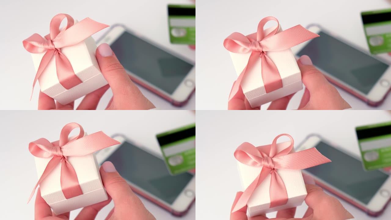 使用智能手机上的在线银行应用程序并在家中持有借记卡的女性手持礼品礼物盒的特写视图。网上购物。假期礼物