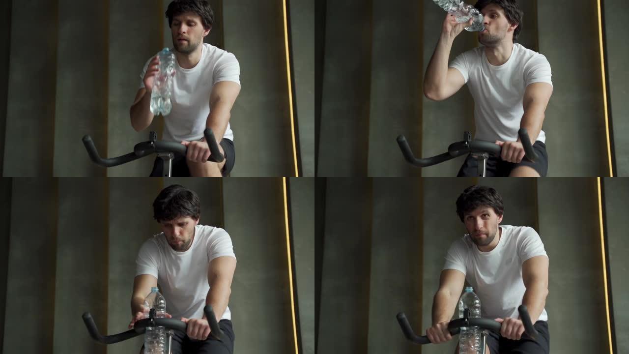 年轻人在健身房喝水。运动员在健身房锻炼自行车