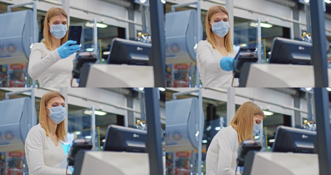 戴着医用口罩的女人在超市的自助结帐柜台付款。女人用智能手机，nfc付款。在检疫期间购物冠状病毒，新型