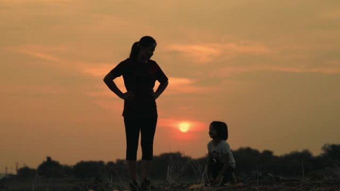 母亲和女儿在日落时在湖上从事瑜伽。家庭深情的关系概念。