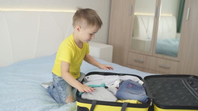 一个可爱的男孩打开一个黄色的手提箱，检查他是否把一切都带到了海上度假