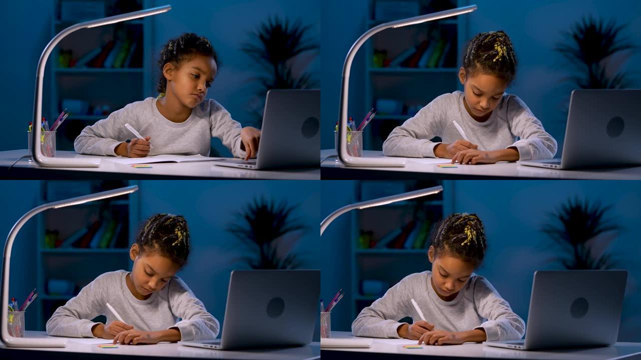 疲惫的女孩不情愿地从笔记本电脑上重写任务。一个非洲裔美国女孩坐在黑暗房间的桌子旁，靠台灯的光。特写。