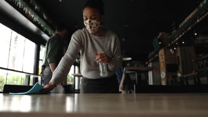 咖啡馆里有带消毒剂的口罩清洁桌的女服务员