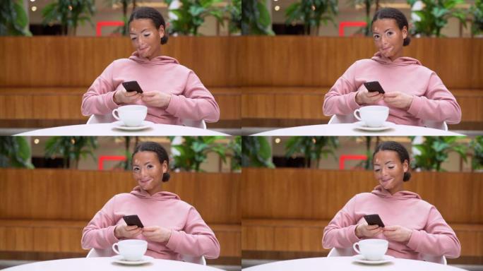 患有白癜风色素沉着皮肤问题的黑人非洲裔美国女性室内穿着粉色连帽衫使用智能手机