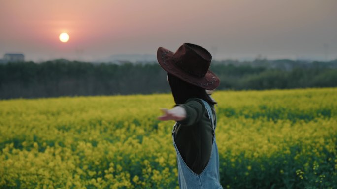 牛仔帽背带裤女生在夕阳下油菜花田间奔跑