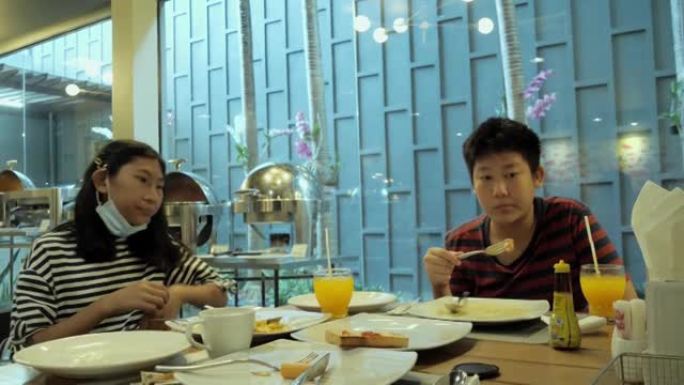 快乐的亚洲儿童在度假期间与家人一起在酒店附近的自助餐厅一起吃早餐，生活方式理念。