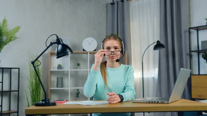 在线视频会议后，戴着耳机的20岁女孩在相机上拍照，一边摘下眼镜，一边微笑着可爱的肖像