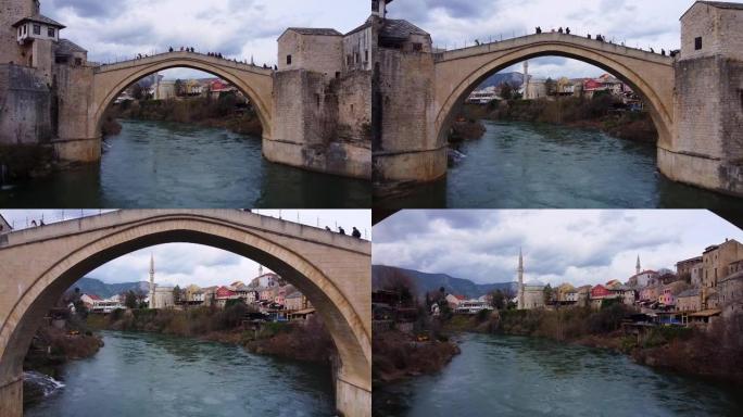 人们在古镇两岸之间的山河上的历史拱形石桥上行走，在桥跨下多云的天空飞行下