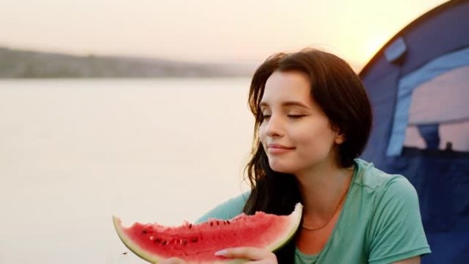 在日落的野餐特写镜头上，美丽的女人带着一大块西瓜享受着大自然的时光。在阿里·阿列克谢拍摄
