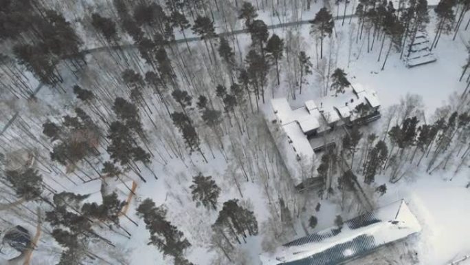 森林中的一块地块，其中隐藏着一座神秘的豪宅，其屋顶被雪覆盖。无人机在冬天飞过。冬季景观中的房屋