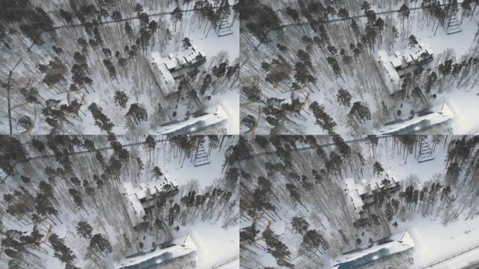 森林中的一块地块，其中隐藏着一座神秘的豪宅，其屋顶被雪覆盖。无人机在冬天飞过。冬季景观中的房屋