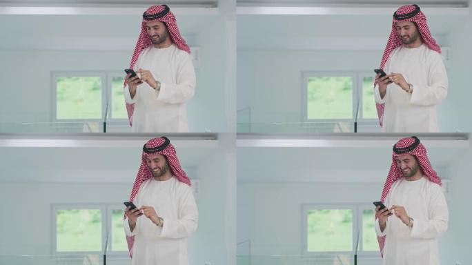 阿拉伯商人穿着传统服装，在家里使用智能手机