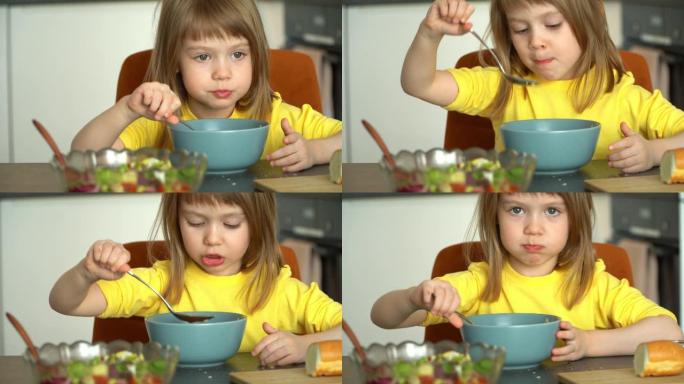 孩子坐在餐桌旁，在厨房里喝汤。小女孩吃番茄汤配面包丁和奶酪。