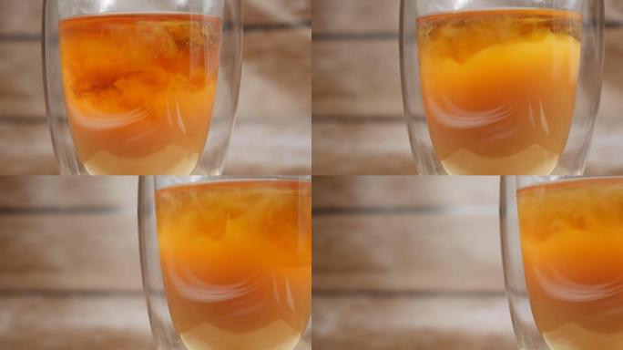 牛奶被添加到茶中。通过双层玻璃烧杯特写镜头。拍摄多莉。