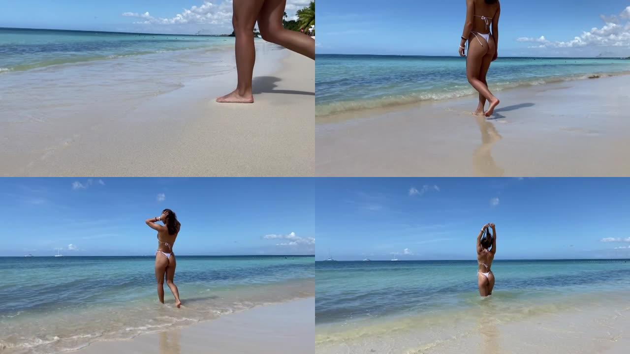 穿着白色比基尼的性感健美女人在海滩边走到水晶水边。旅行、健康和幸福的概念