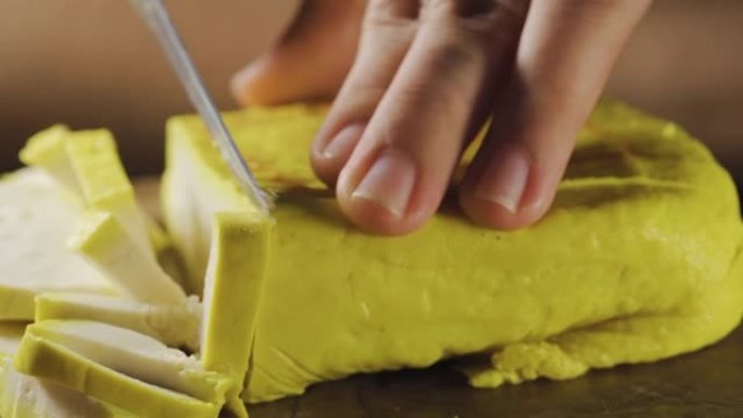 黄色豆腐在木板上切片。特写。在微距拍摄中准备烹饪。中国传统成分。泰国菜。