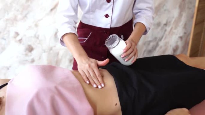按摩治疗师在按摩院的女性客户的肚子上涂抹椰子油。