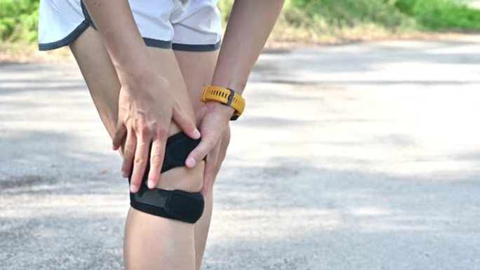 在过度训练的情况下，跑步者妇女抱着膝盖并做膝盖按摩的特写镜头。