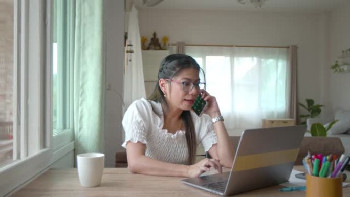 年轻的亚洲女性在检疫Covid 19大流行期间，在电脑笔记本电脑上滚动搜索社交媒体上的数据，并在家工
