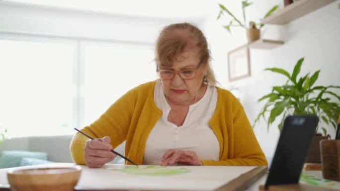 退休妇女使用智能手机进行水彩画在线课程