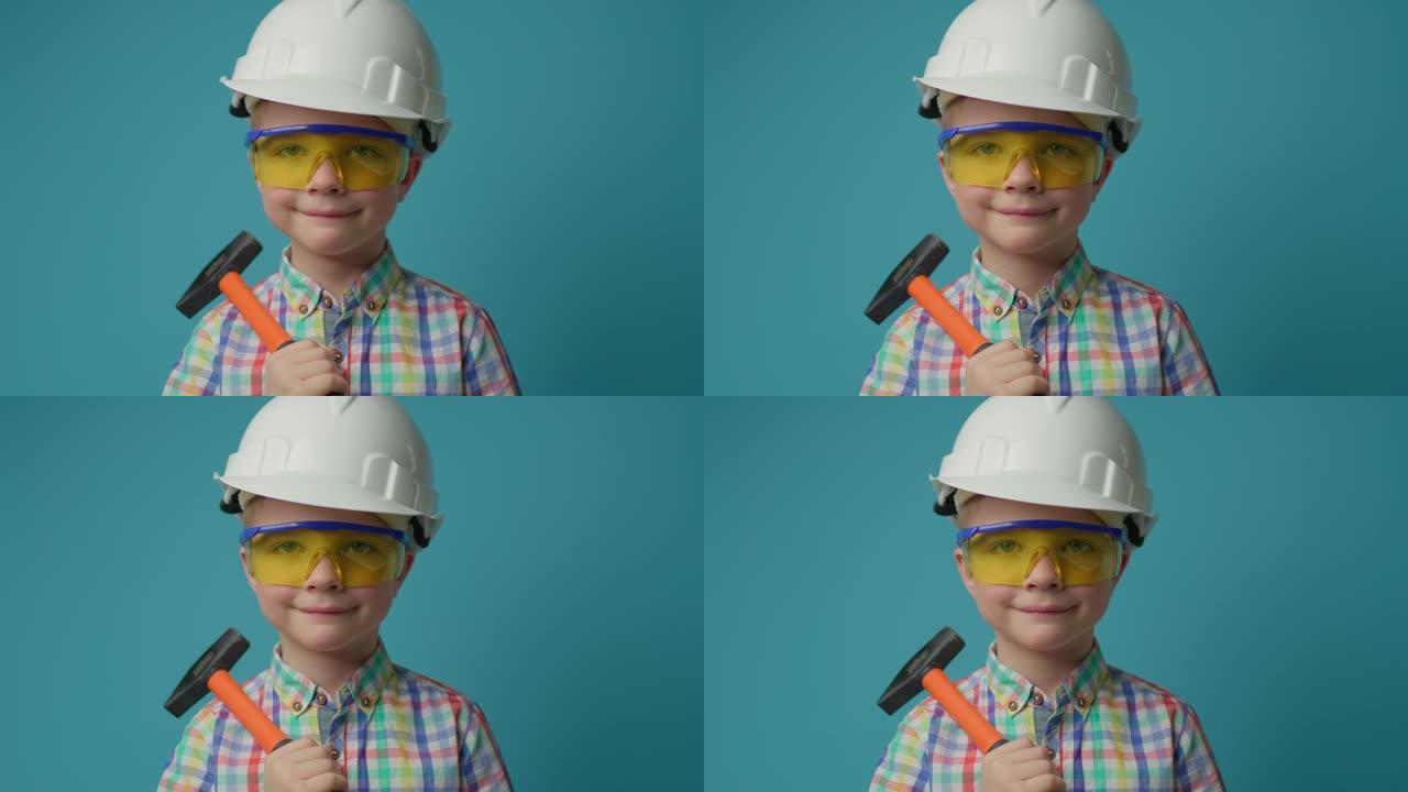 戴着白色安全帽和防护眼镜的小男孩手里拿着悍马微笑着看着蓝色背景的相机。