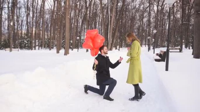 年轻人跪下，在冬天的一个公园里向他美丽的年轻女子求婚