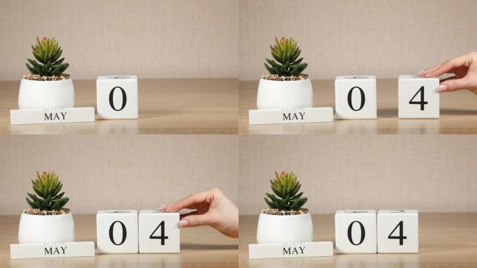 木制日历对5月04日来说是一个重要的事件，女人的手在日历上设置日期。春季。