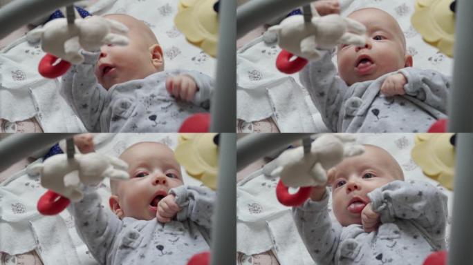 2个月大的婴儿脸部特写，可爱的男婴躺在活动健身房游戏垫上玩悬挂玩具，婴儿感官发育