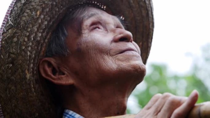 一个高兴的亚洲老人站在花园里，面向天空的特写镜头。农民对季节下雨感到高兴。