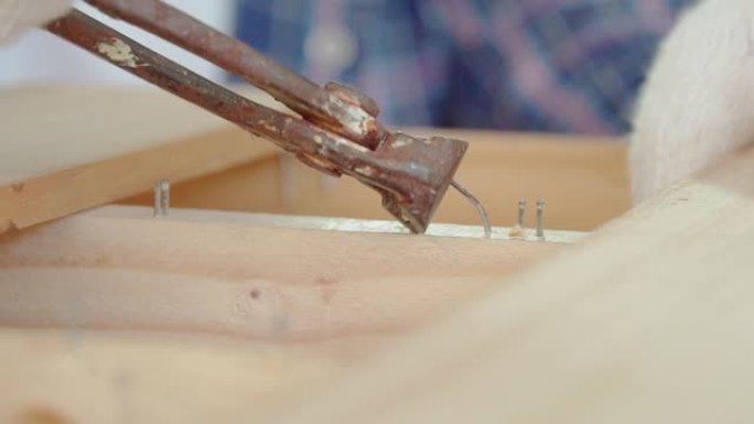 一个木匠正在用钳子拔钉子。木匠锤入木板后用钳子取出钉子。
