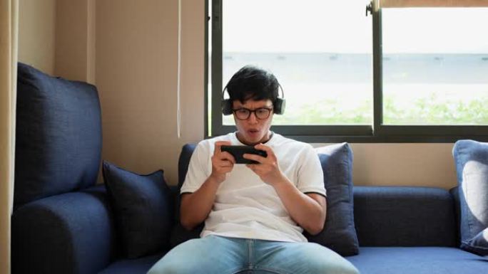 慢动作场景少年亚洲男子坐在客厅，用智能手机在网上玩游戏锦标赛最后一轮，成为生活方式技术概念的赢家后感