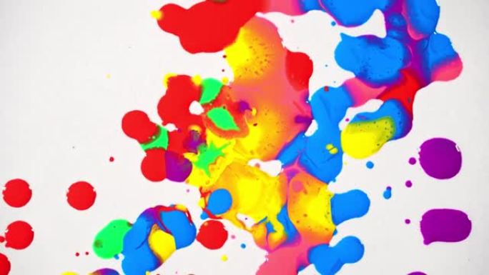 各种颜色的油漆的俯视图滴在白纸上并旋转成圆圈，颜色融化在一起。