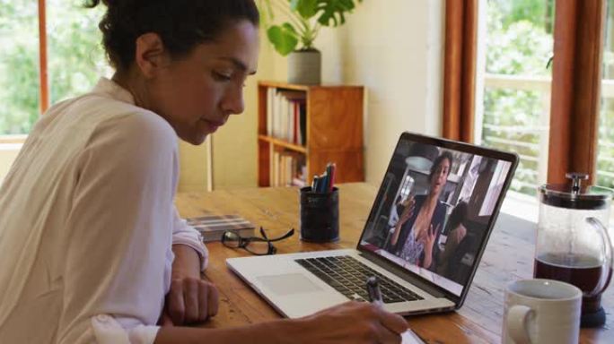 非裔美国妇女在家里用笔记本电脑与女同事进行视频通话时做笔记