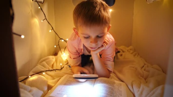 小聪明男孩晚上读大故事的肖像。在玩具纸板屋玩耍的孩子。儿童教育与暗室阅读的概念