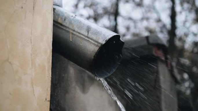 排水管的侧视图，水从该排水管在沥青上流动。城市大雨