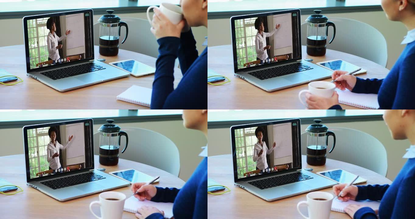 高加索女教师在笔记本电脑上进行视频通话时喝咖啡并做笔记