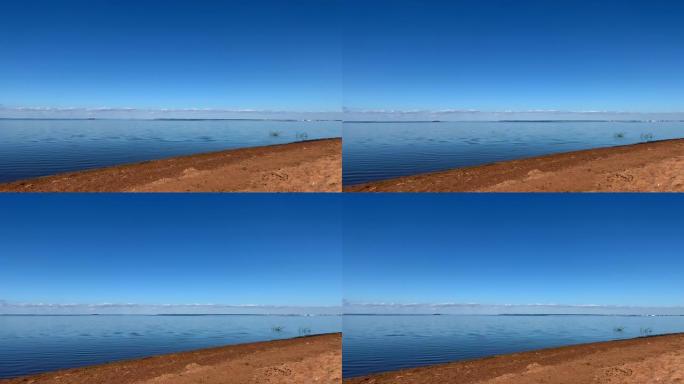 非常蔚蓝的大海、蓝天和橙色的沙子。在地平线上可以看到小云。风无浪水面有小涟漪